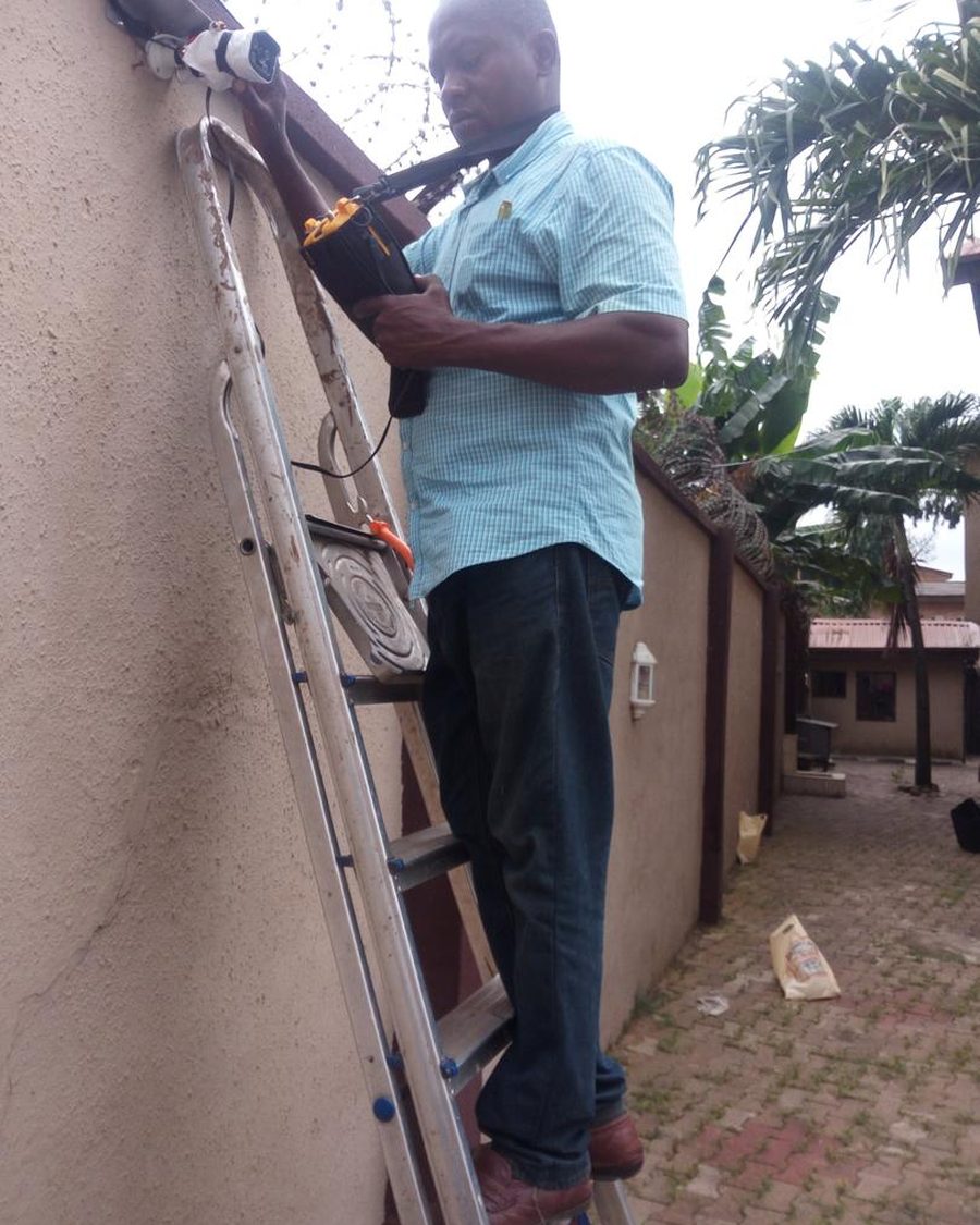 A Trewbless technician on a ladder adjusting a CCTV bullet camera on a perimeter wall.